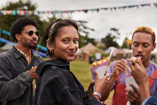 Woman eating waffle cone wearing black denim jacket and smiling at party