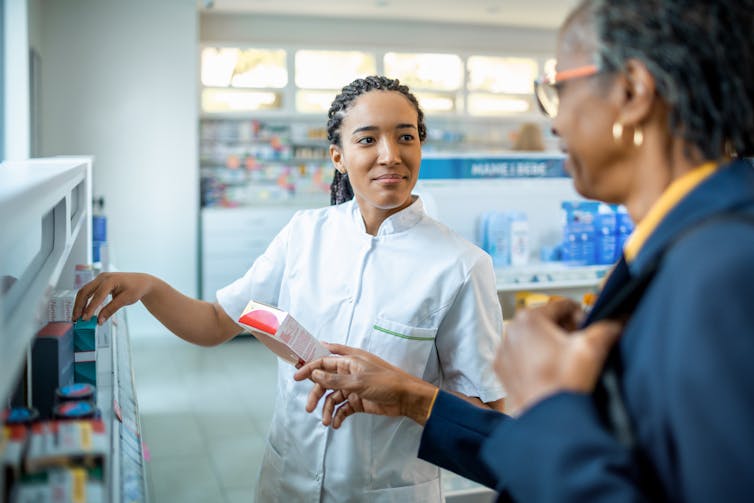 A black female pharmacist shows a Black woman some prescription drugs.